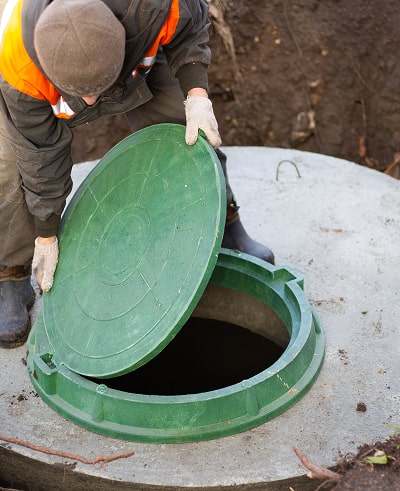Man in safety gear opening a green septic tank cover.