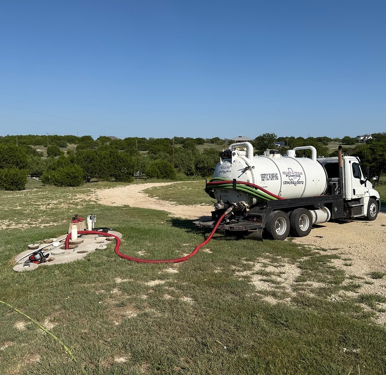 White septic truck parked on a dirt road, pumping a septic tank.