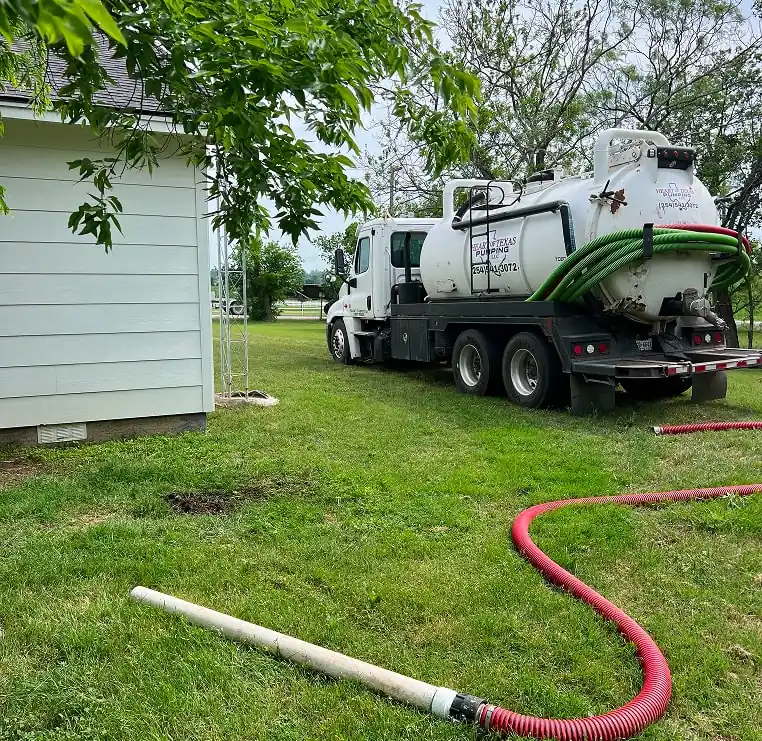 White septic truck parked beside a house with hoses on the ground.